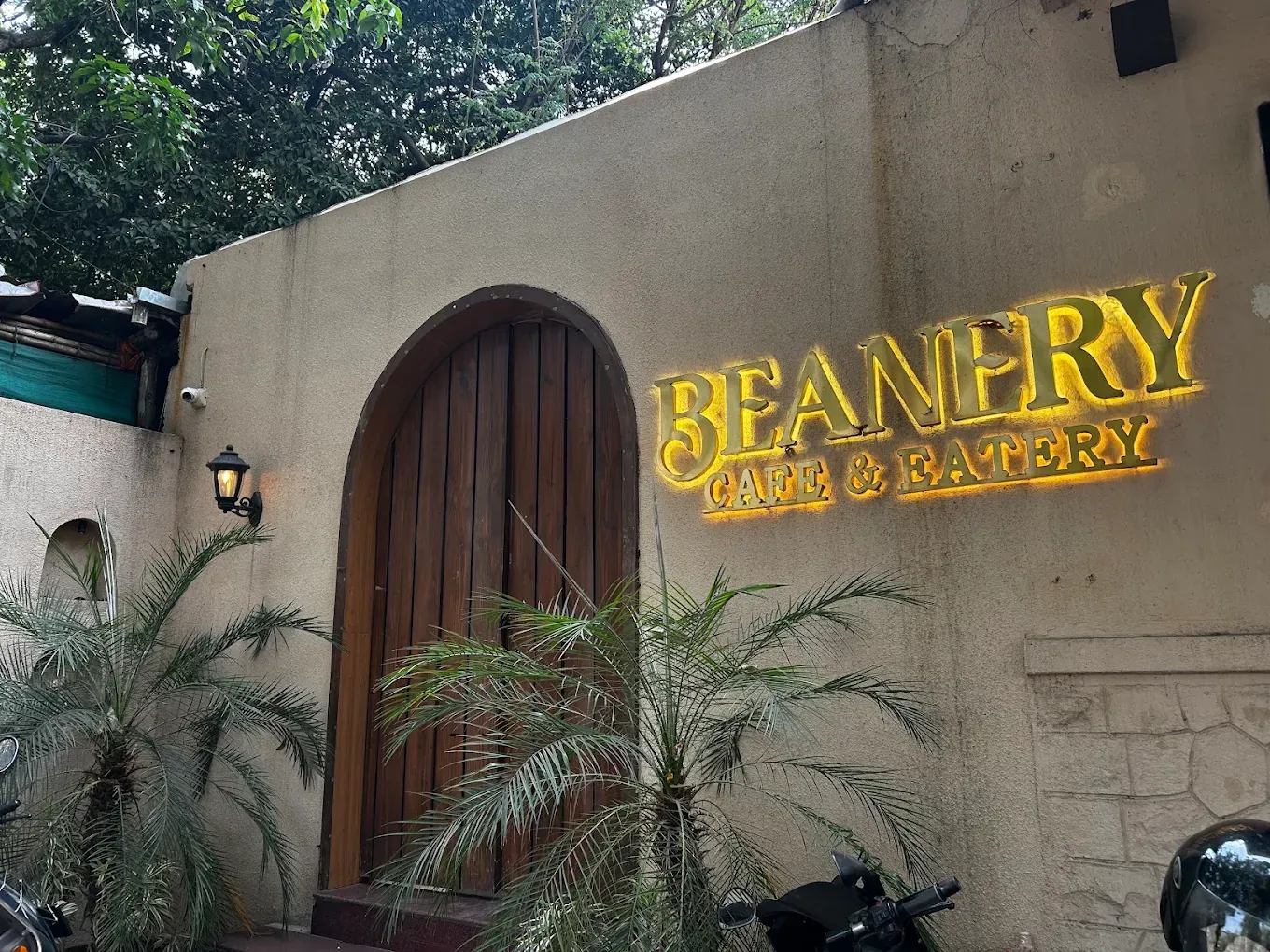 Beanery Café arched entrance with an illuminated sign and plants.