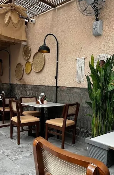 Cafe table beside plants, woven wall baskets and a black wall lamp.
