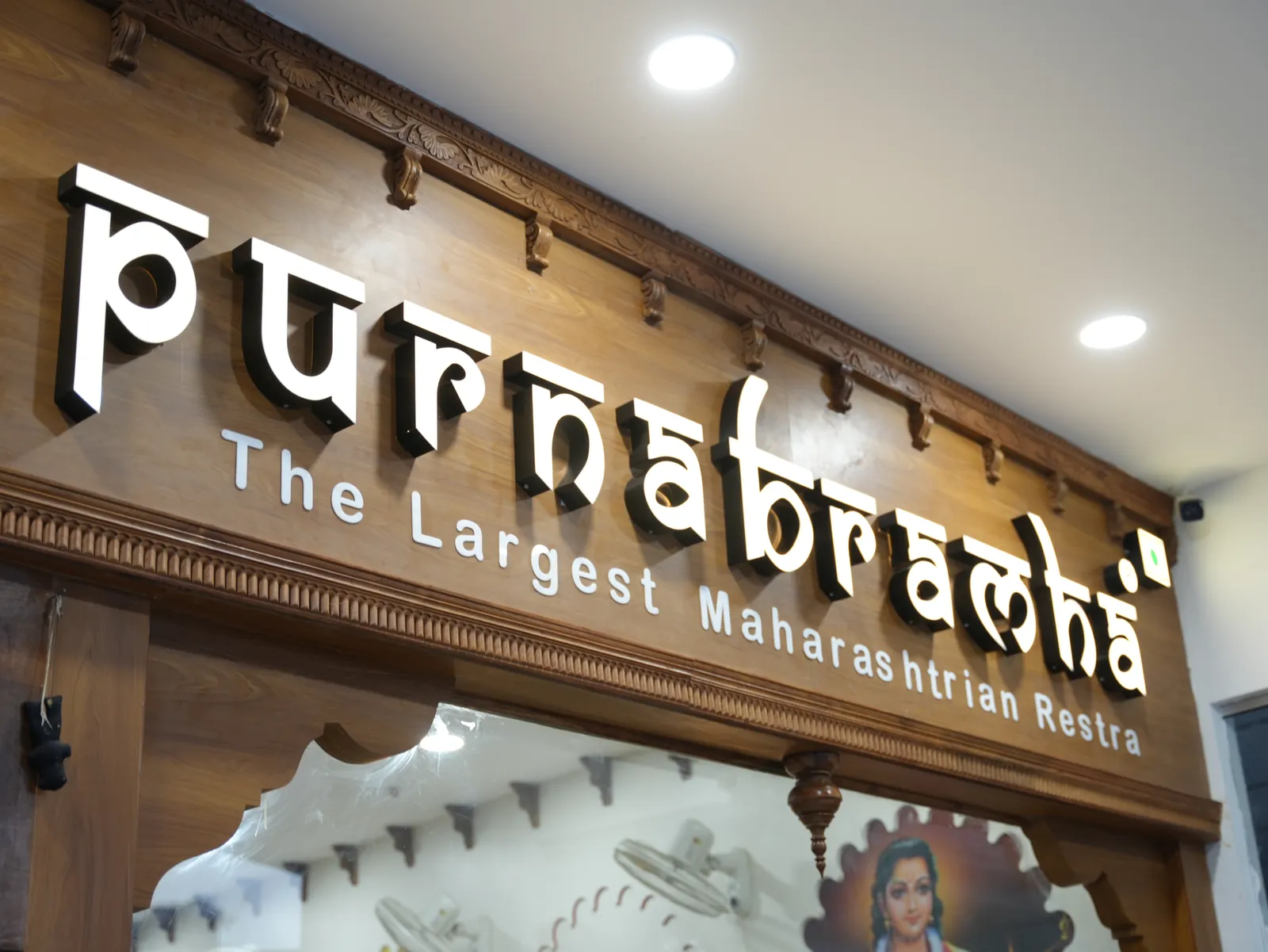 Illuminated Purnabramha sign beneath carved trim above the entrance.