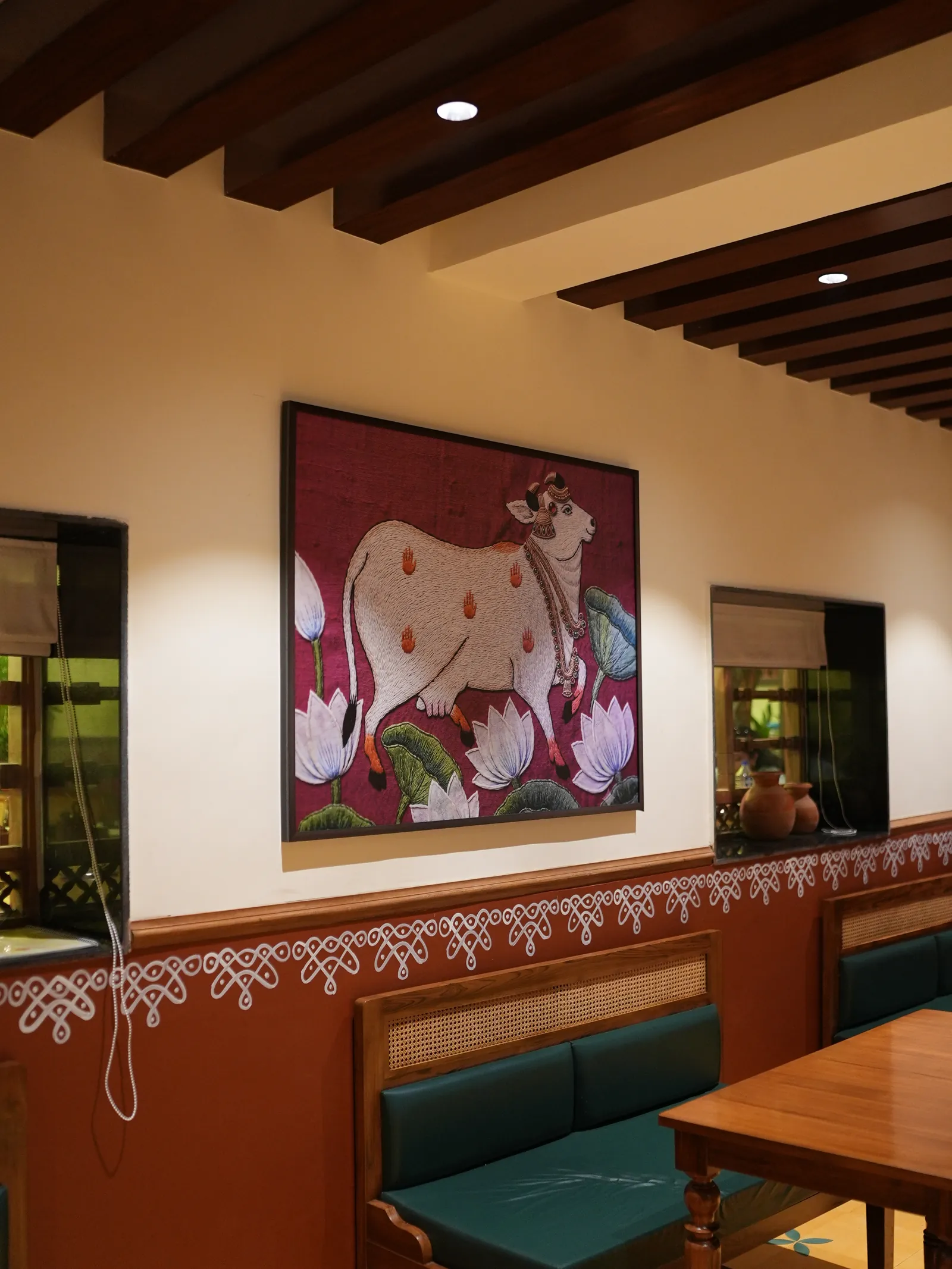 Green dining banquette below cow-and-lotus artwork, a patterned wall border and ceiling beams.